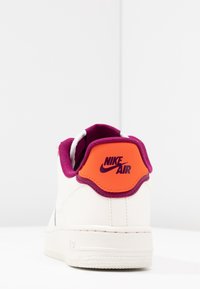 Sneaker bianca con colletto imbottito in bordeaux e targhetta arancione sul tallone con il logo "Nike Air". Suola in gomma testurizzata per una buona aderenza.