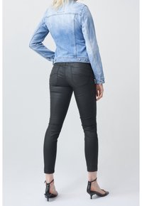 Džínová bunda se světle modrým přechodem, přiléhavé černé skinny džíny a černé sandály na podpatku, pohled zezadu na neutrálním pozadí.