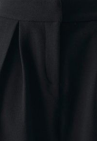 Tissu noir texturé avec un design plissé, présentant une silhouette épurée et une finition lisse. Le matériau semble doux et structuré.