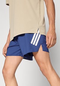 Kék atlétikai rövidnadrág fehér csíkokkal az oldalán, könnyű anyagból készült, hasított szegéllyel a jobb mozgékonyság érdekében.