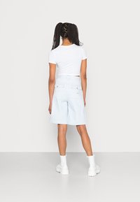 Pantalones cortos de mezclilla azul claro con un ajuste relajado, que cuentan con bolsillos traseros y un desgaste sutil, combinados con una camiseta blanca ajustada y botas blancas.