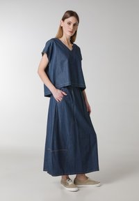 Denim kaksiosainen asu, joka sisältää lyhyttukkaisen, V-pääntiellä varustetun paidan ja pitkän hameen, jossa on sivutaskut. Tumma sininen kangas, jossa on kontrastivärisiä ompeleita.