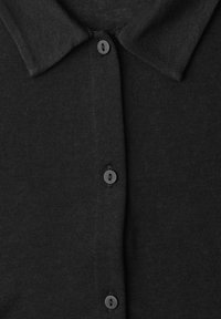 Chemise en maille noire avec col et quatre boutons ronds noirs au centre devant.