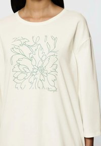 Kremowa, długosleeve koszula z zielonym wzorem kwiatowym na konturze oraz słowem "Triumf" w prawym dolnym rogu. Miękka, gładka tkanina.