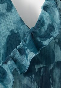 Modro barvano blago z navpično rebrasto teksturo in nabranim robom, ki prikazuje gube in naravne sence zaradi svetlobe.