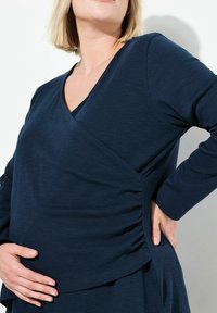 Marineblaues, langärmliges Stilloberteil mit V-Ausschnitt, seitlichem Rüschendetail und lockerem Schnitt. Hergestellt aus weichem, dehnbarem Material.