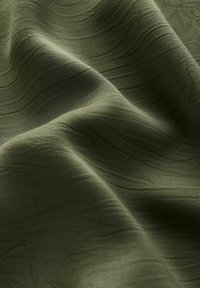 Tessuto verde texturizzato con sottili modelli a onda, finitura morbida e aspetto liscio. Il materiale appare leggero e flessibile.