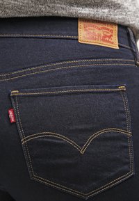 Tamno plave traperice s žutim šavovima, s leđnim džepom zakrivljenog dizajna i smeškim kožnim Levi's oznakom.