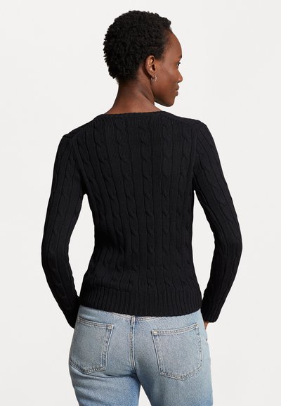 Pulover negru din tricot cu un design ajustat, cu manșete și tiv zimțate, asortat cu blugi de culoare albastră deschisă. Materialul pare texturat și gros.