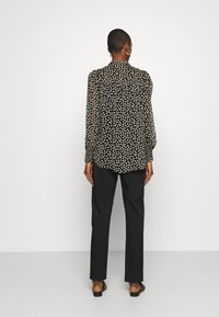 Blusa nera trasparente con pois bianchi, collo alto, maniche a sbuffo e polsini elastici. Abbinata a pantaloni neri aderenti e sandali.
