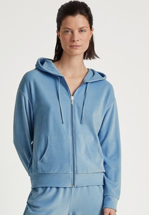 Felpa con zip di colore azzurro chiaro realizzata in tessuto morbido, dotata di cappuccio, tasche frontali e una vestibilità rilassata con polsini e orlo a costine.