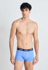 Boxer-briefs bleus avec une bande sombre portant l'inscription "HUGO". Fabriqués dans un tissu lisse, avec une coupe ajustée et une longueur de jambe courte.
