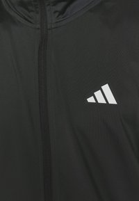 Sort atletisk jakke med høj krave, lynlås lukning og et hvidt tre-stripes logo på venstre bryst. Glat stof tekstur.