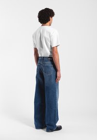 Relaxed-fit blue denim jeans with a high waist and wide legs, paired with a plain white t-shirt, viewed from the back.