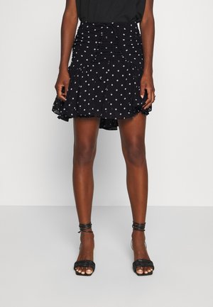 Woman wearing a black mini skirt with white polka dots and ruched front, paired with black strappy high-heeled sandals.