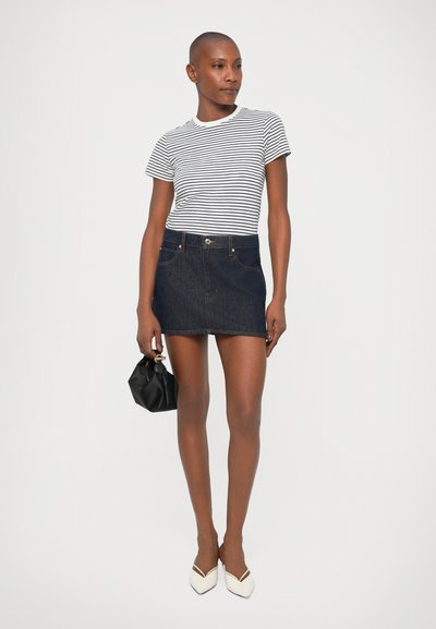 Tricou cu mânecă scurtă cu dungi, alb cu linii negre; fustă mini din denim închis la culoare cu buzunare frontale și închidere cu buton; pantofi plate albi și geantă neagră.