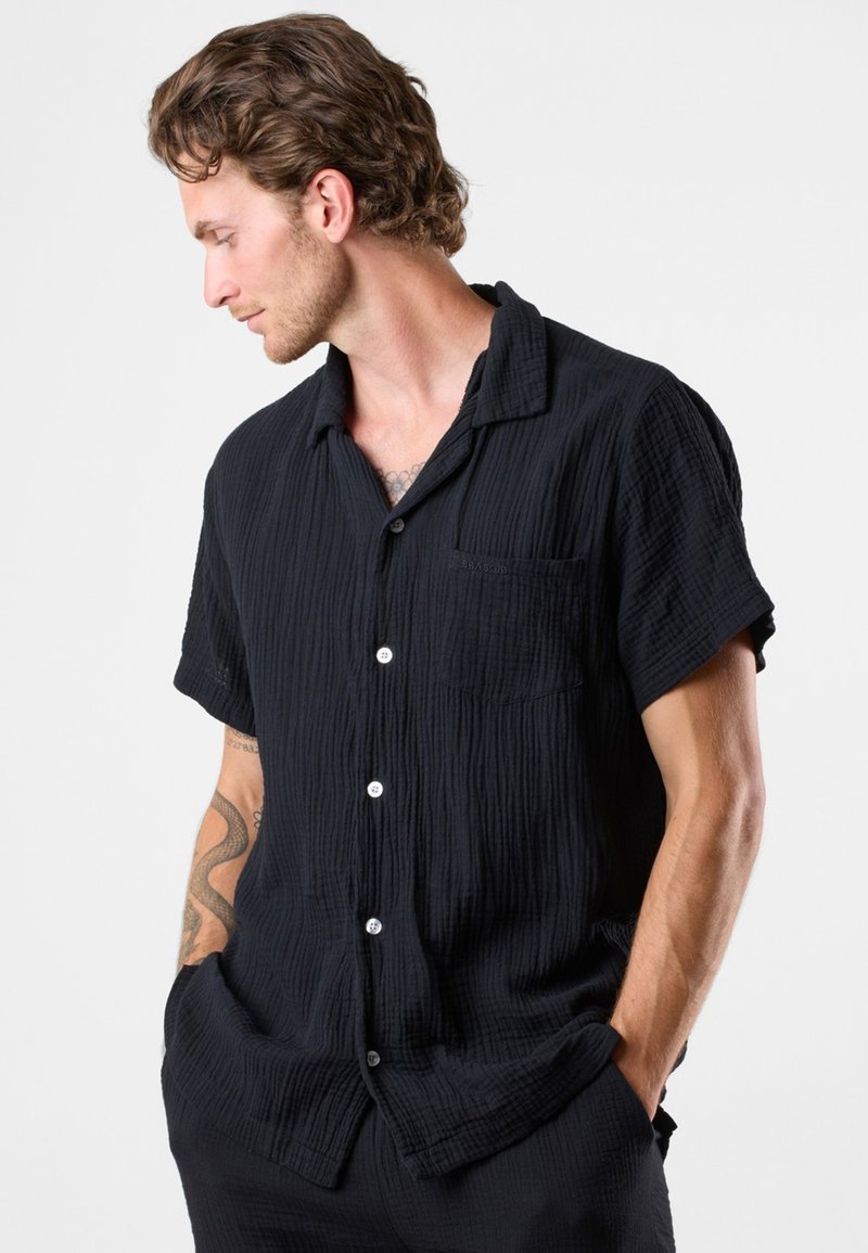 Chemise noire à manches courtes en tissu texturé, dotée d'un devant à boutons, d'une poche poitrine unique et d'une coupe décontractée avec un col.