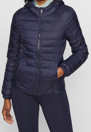 Chaqueta acolchada azul marino con capucha, que presenta un diseño de acolchado horizontal, cremallera frontal y puños elásticos. Lleva puesta sobre pantalones oscuros.