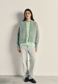 Lichtgroene gebreide cardigan met verlengde mouwen, gecombineerd met een mintgroen T-shirt en lichtgewassen rechtkleurige jeans. Zwarte loafers maken de look compleet.