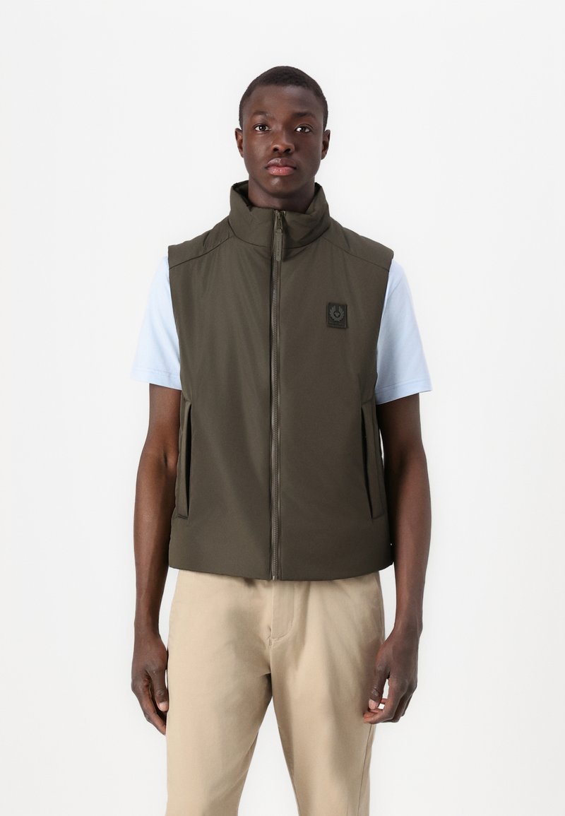 Olive green, sleeveless jacket with high collar, front zipper, and side pockets. Features a small logo on the chest. Pairing with light shirt.