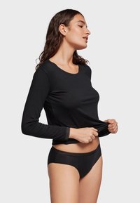 Zwarte langmouwtop met een ronde halslijn en een getailleerd ontwerp, gecombineerd met zwarte bikini-ondergoed met een kantafwerking.