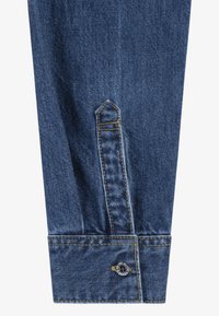 Cuff di camicia in denim con chiusura a bottone, caratterizzato da cuciture gialle a contrasto e un taglio triangolare. Tessuto blu scuro con texture liscia.