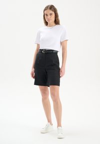 Czarne szorty z wysokim stanem z przednimi kieszeniami, zestawione z białą koszulką i czarnym paskiem. Białe sneakersy dopełniają zestaw.