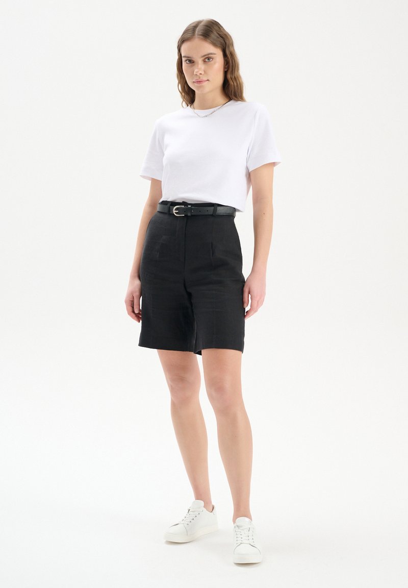 Czarne szorty z wysokim stanem z przednimi kieszeniami, zestawione z białą koszulką i czarnym paskiem. Białe sneakersy dopełniają zestaw.