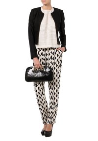 Giacca aderente nera sopra una maglia bianca strutturata, abbinata a pantaloni con motivo geometrico bianco e nero e una borsa nera lucida.
