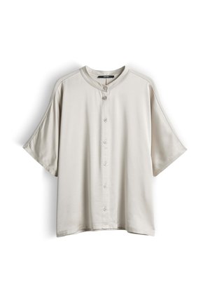 Camicia beige chiaro a maniche corte con colletto tondo e sette bottoni sulla parte anteriore, mostrata su uno sfondo bianco.