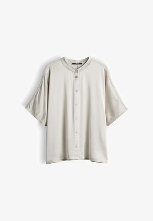 Camicia beige chiaro a maniche corte con colletto tondo e sette bottoni sulla parte anteriore, mostrata su uno sfondo bianco.