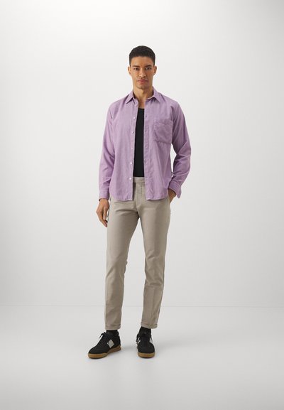 Hellblaues button-up Hemd mit einer Brusttasche, kombiniert mit beigen Hosen und schwarzen Sneakers mit Gummisohle. Enganliegendes Design.