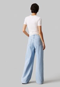 Helle blaue weite Jeans mit hoher Taille und zwei Gesäßtaschen, kombiniert mit einem enganliegenden weißen Rippt-Shirt. Lässig und entspannt geschnitten.