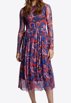 Woman wearing a long-sleeve, knee-length dress with a swirling abstract pattern in red, blue, and pink colors.