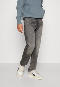 Grå denimjeans med en blekt finish, kombinerade med en blå hoodie och beige sneakers. Jeansen har en rak passform och en subtil textur.