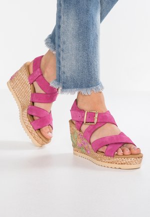 Sandales compensées en suède rose avec des lanières croisées et une boucle, présentant une base en jute tissée et un détail de broderie florale sur le talon.