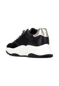 Zapatilla deportiva negra con parte superior de malla texturizada, detalles de cuero, talón metálico y una suela blanca gruesa con un dibujo negro rugoso.