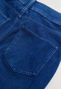 Gros plan sur un tissu en denim bleu foncé montrant la poche arrière et les coutures de la ceinture d'un jean.
