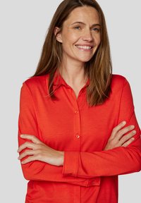 Red button-up shirt made of smooth fabric, featuring a collared neckline and long sleeves, with a relaxed fit and no visible patterns.