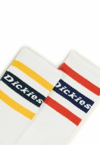 White ribbed socks featuring horizontal stripes in yellow, red, and navy, with the brand name "Dickies" woven in contrasting colors.