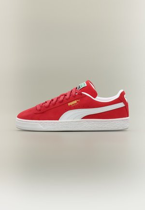 Κόκκινο sneaker Puma από σουέντ με λευκή ρίγα Puma, λευκή σόλα, κορδόνια και πράσινο λογότυπο στη γλώσσα, εμφανίζεται πλευρική όψη σε ουδέτερο φόντο.