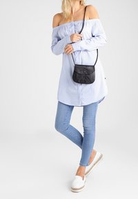 Ljusblå off-shoulder skjorta med långa ärmar och utan krage, kombinerad med ljusblå tajta jeans och vita espadrillos, kompletterad med en liten svart väska.