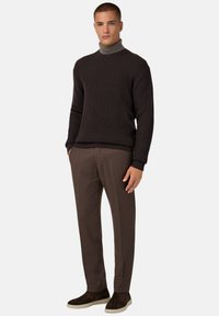 Pull en maille côtelée sombre avec un col haut, associé à un pantalon marron ajusté et des mocassins en suède marron. Textures lisses, coupe moderne.