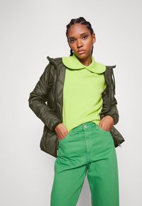 Vadderad olivgrön jacka, ljus limegrön tröja och djärva gröna jeans. Har en stor krage och rak benklipp.