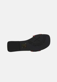 Suola di scarpa in gomma nera con strisce di accento rosse, caratterizzata da un marchio in rilievo e simboli di cura, design piatto e una superficie liscia.