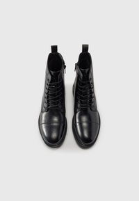 Botas de tobillo de cuero negro con un diseño elegante, que cuentan con cordones en la parte delantera y cremallera lateral, punta redonda y textura suave.