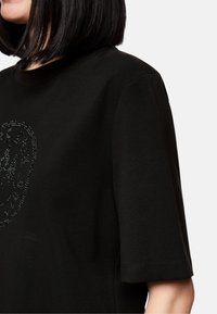 Black cotton t-shirt with a round neckline and short sleeves, featuring a textured rhinestone design on the front. Soft, casual fit.