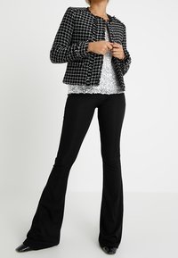 Czarna i biała marynarka tweedowa o skróconym fasonie, postrzępionych brzegach i okrągłym dekolcie. Nosi się ją na cekinowej bluzce oraz czarnych szerokich spodniach.