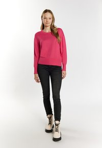 Rózsaszín kötött pulóver kerek nyakkivágással, fekete skinny farmerral és krémszínű fűzős csizmával, fekete talppal párosítva. Minimalista stílus.
