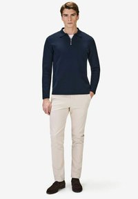 Marindras dragkedjepullover i mjukt trikåtyg, kombinerad med ljusbeiga slim-fit byxor och mörkbruna loafers. Enkel, modern design.